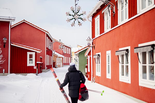 Een persoon met ski's, loopt over een met sneeuw bedekte straat. Foto Hilla Aspman/imagebank.sweden.se